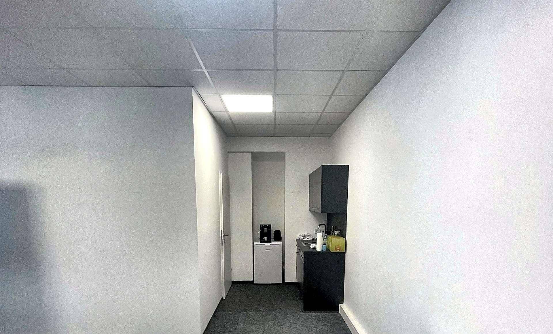 Kleiner Küchenbereich mit dunklen Schränken, Kühlschrank und Kaffeemaschine in einem Flur.