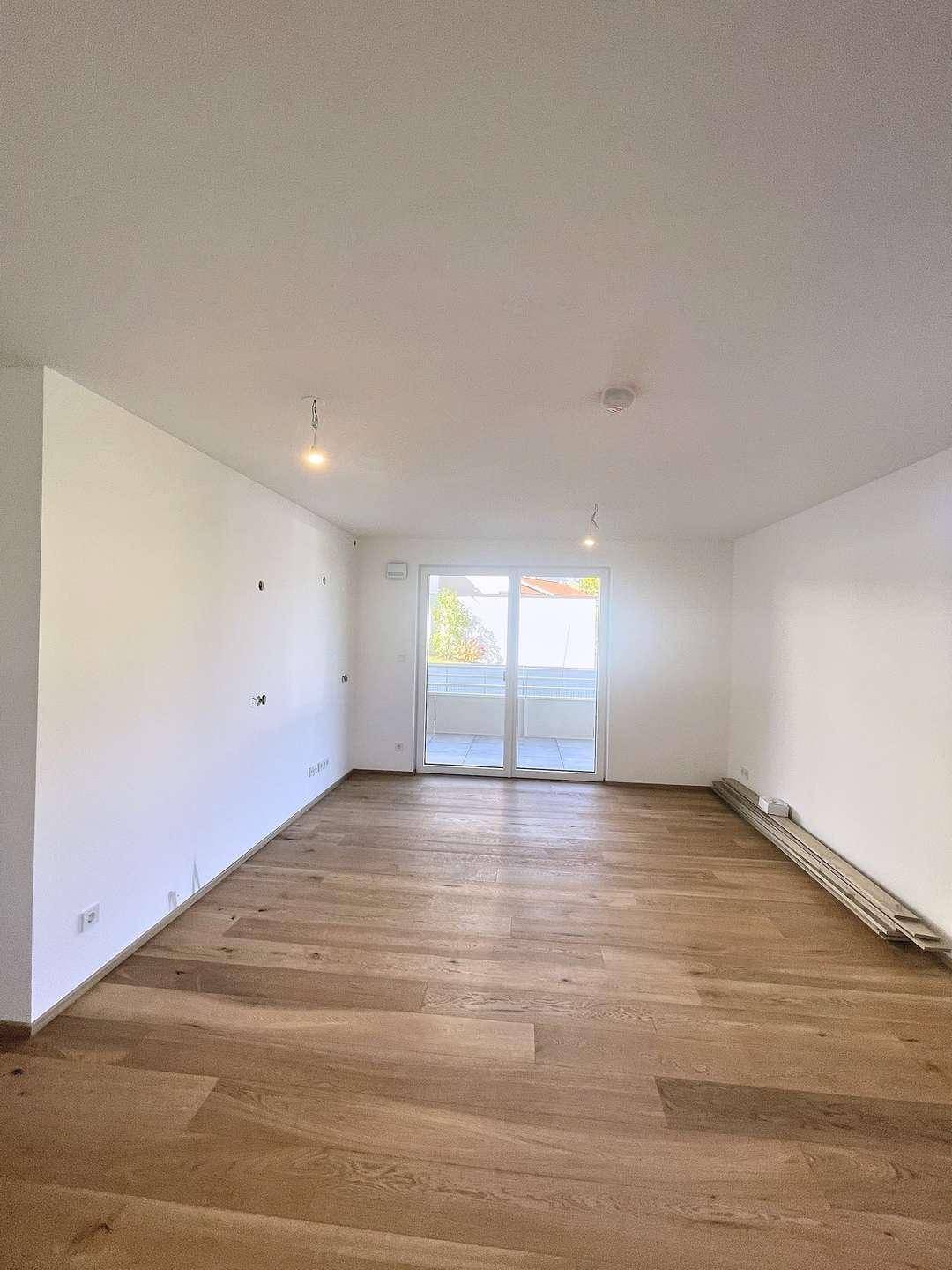 Geräumiges Wohnzimmer mit Holzboden und Zugang zu einem Balkon oder einer Terrasse.