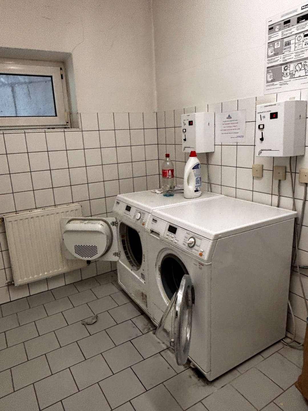 Gemeinschaftlicher Waschraum mit Waschmaschinen und Trockner, gefliesten Wänden und Boden.