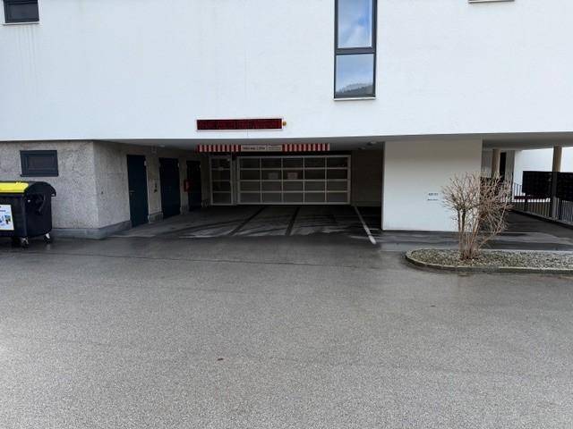 Einfahrt zu einer Tiefgarage unter einem modernen Wohngebäude mit weißer Fassade.