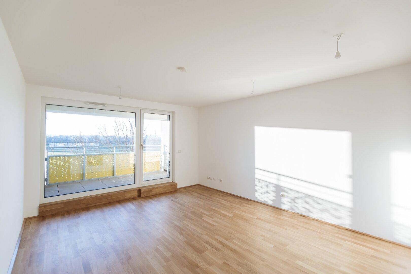 Geräumiges, helles Wohnzimmer mit Parkettboden und großem Fenster zum Balkon.