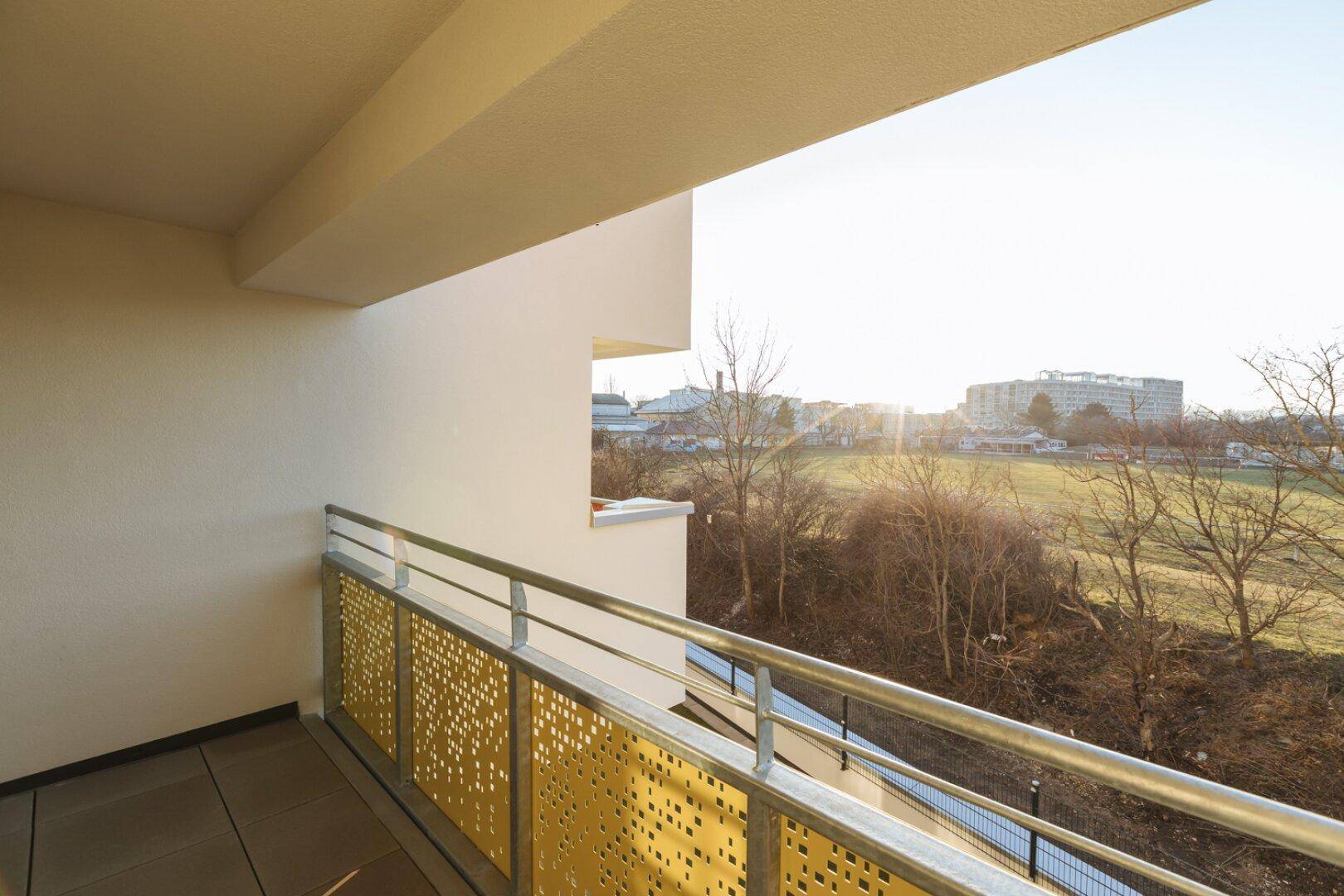 Sonniger Balkon mit moderner Lochblechbrüstung und weitem Blick ins Grüne.