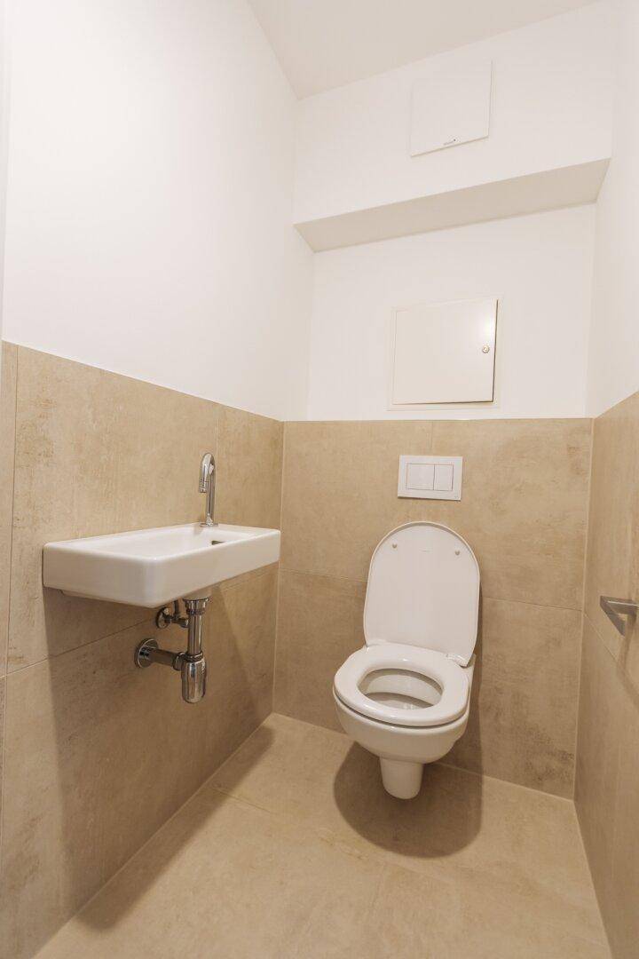 Separates Gäste-WC mit Wand-WC und kleinem Waschbecken, modern gefliest.