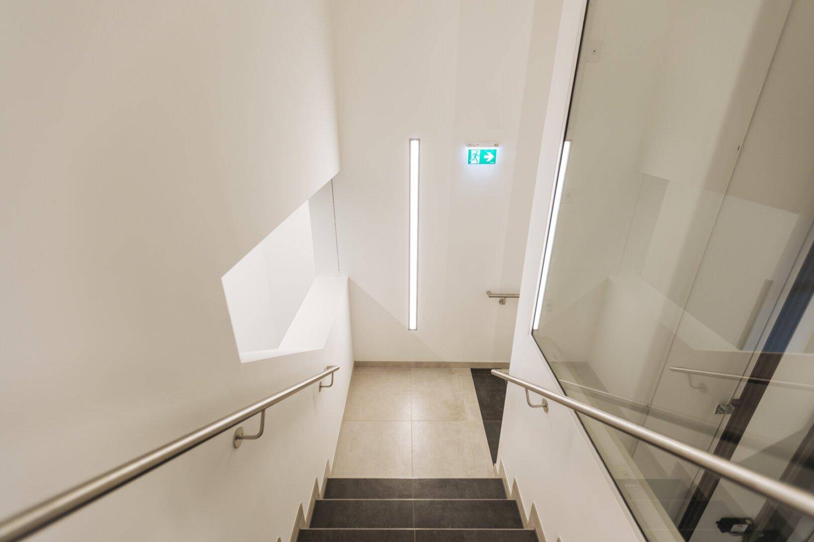 Helles Treppenhaus mit modernen Handläufen und Fliesenboden, gut beleuchtet.
