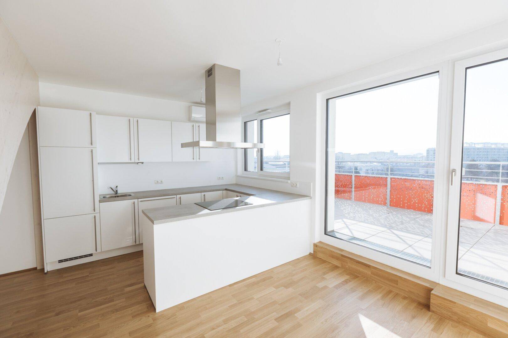 Helle Küche mit weißen Schränken, Kochinsel und Zugang zu einer großen Terrasse mit Stadtblick.