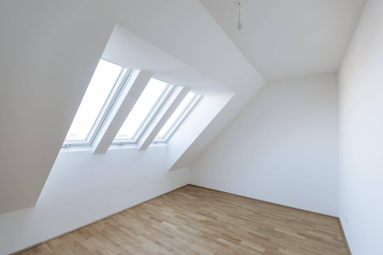 Dachgeschosszimmer mit schrägen Wänden, Holzboden und mehreren Dachfenstern für viel Licht.