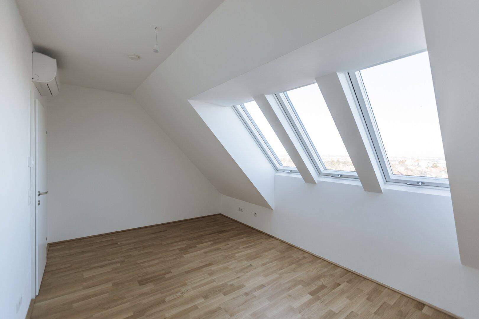 Helles Dachgeschosszimmer mit Holzboden, schrägen Wänden und mehreren Dachfenstern.