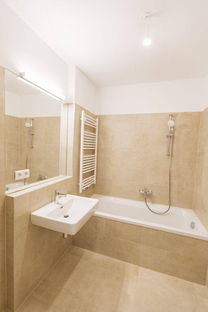 Modernes Badezimmer mit beigefarbenen Fliesen, Badewanne, Waschbecken und beheiztem Handtuchhalter.