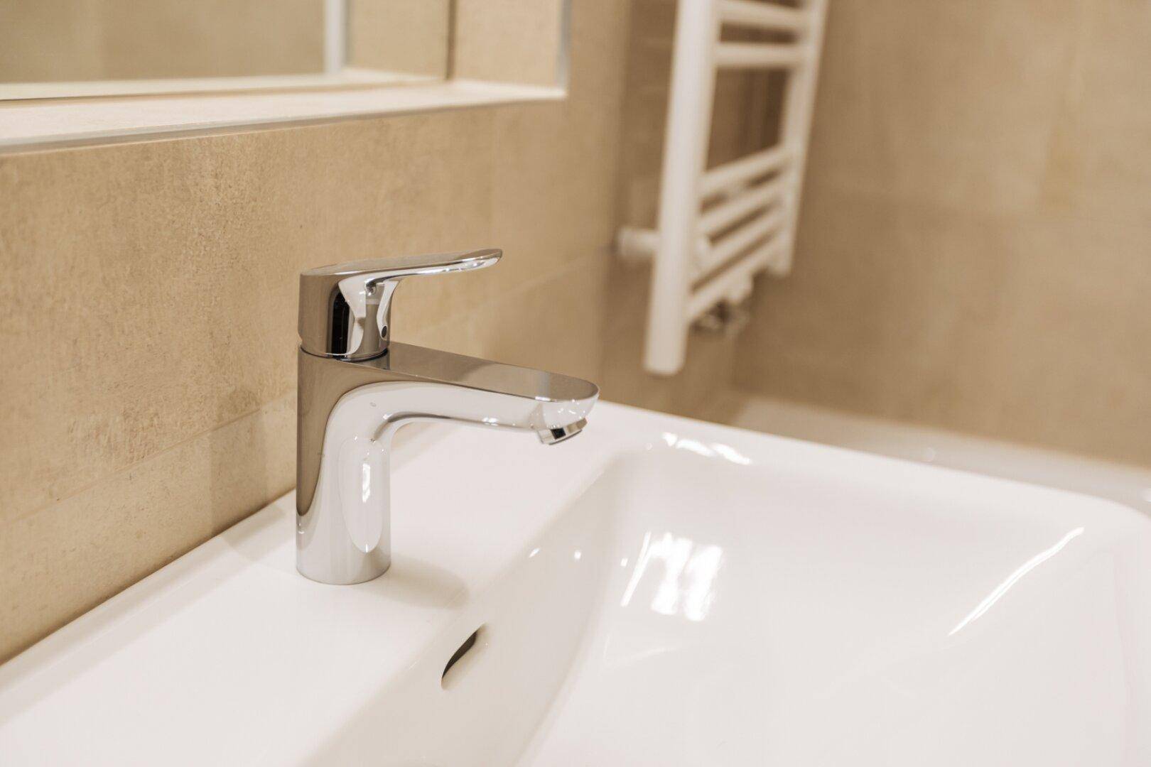 Nahaufnahme eines modernen Wasserhahns aus Chrom über einem weißen Waschbecken im Badezimmer.