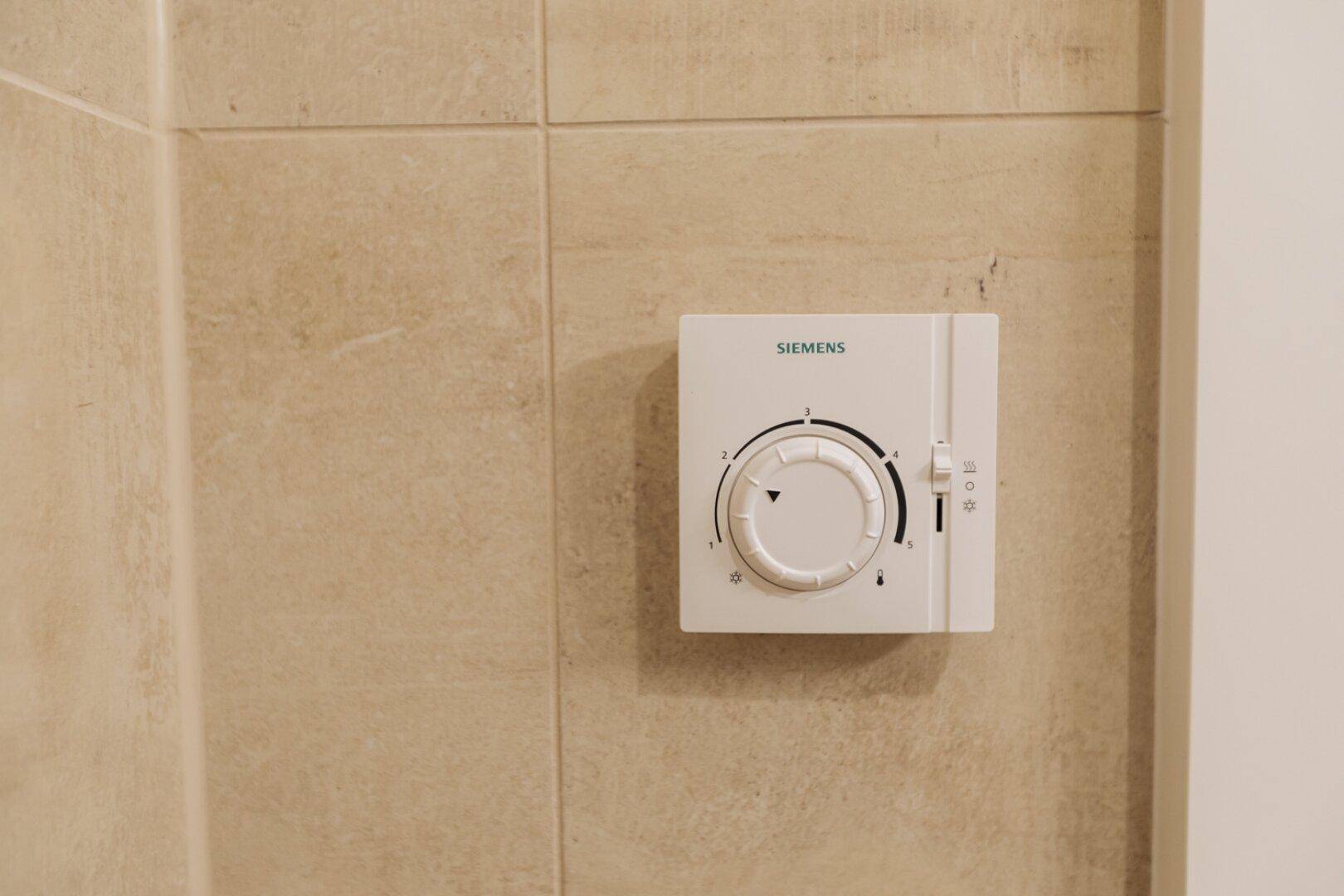 Detailansicht eines Siemens-Thermostats an einer beigefliesten Wand im Badezimmer.