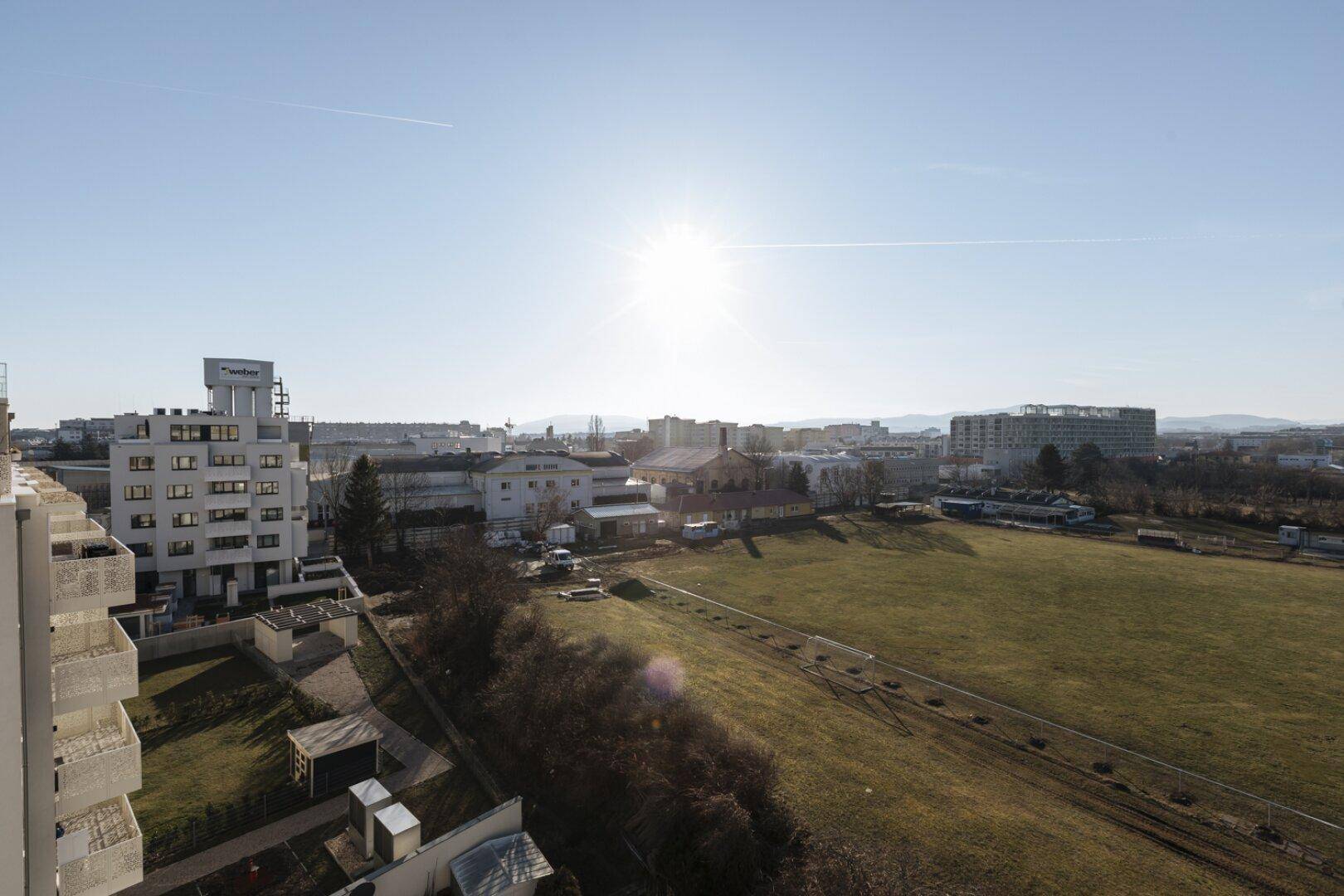 Weitläufiger Blick über eine städtische Landschaft mit Grünflächen und Gebäuden unter strahlendem Himmel.