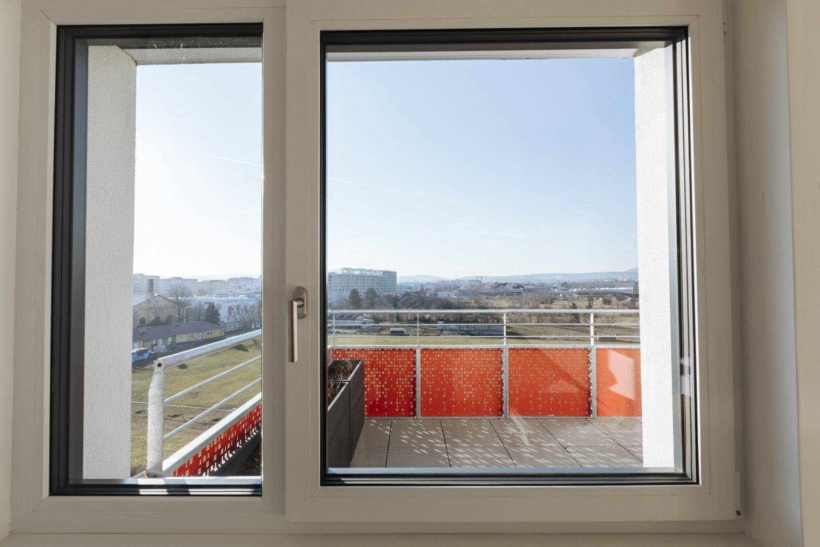 Blick aus einem großen Fenster auf eine Terrasse und die umliegende Stadtlandschaft.