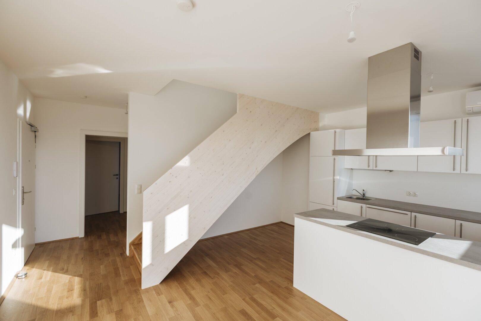 Offene Küche mit Holzboden, Kochinsel und einer modernen Holztreppe, die nach oben führt.