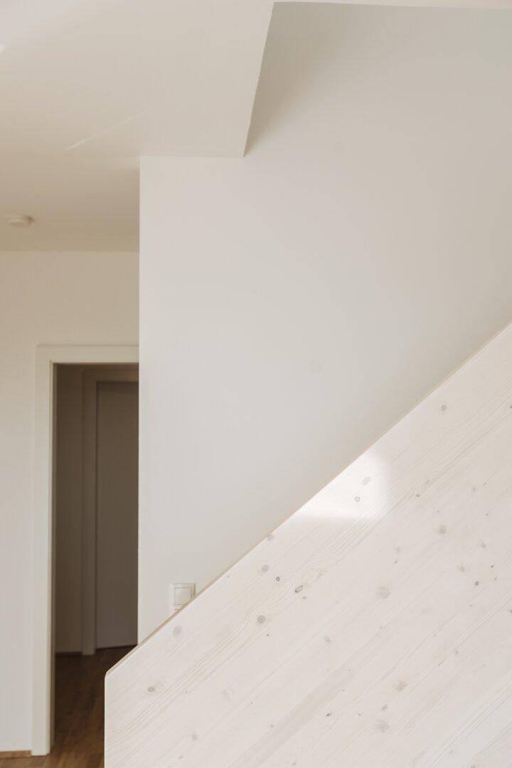 Detailansicht einer modernen Holztreppe mit weißer Wand und natürlichem Lichteinfall.