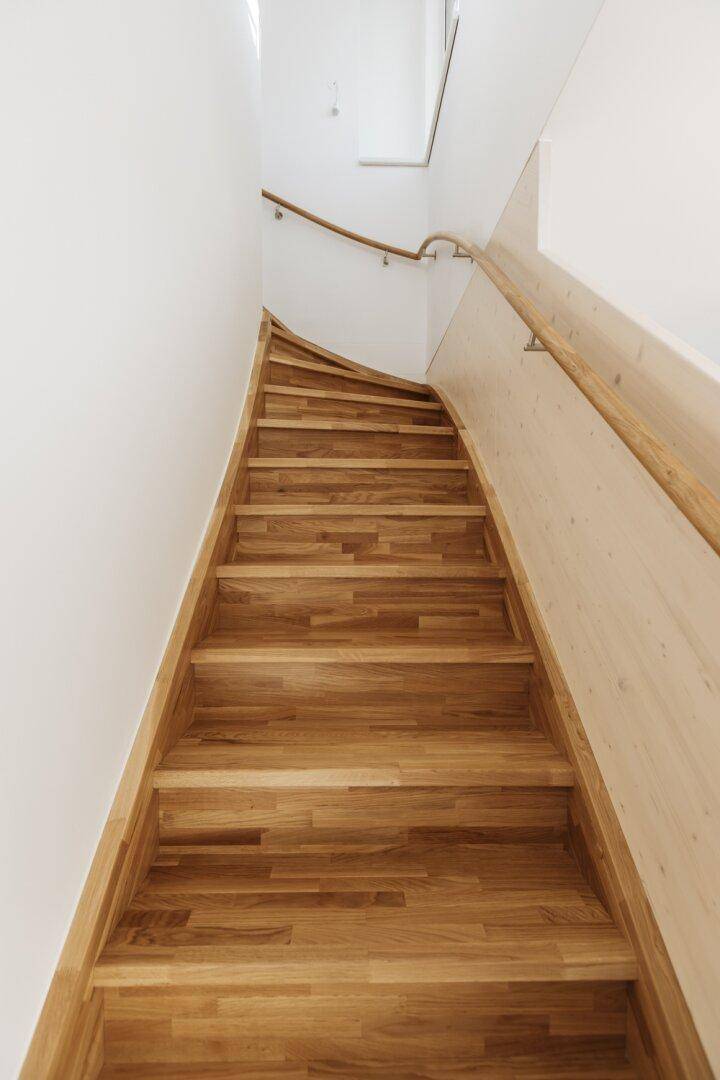 Elegante Holztreppe mit Handlauf und natürlichem Lichteinfall, die in ein oberes Stockwerk führt.
