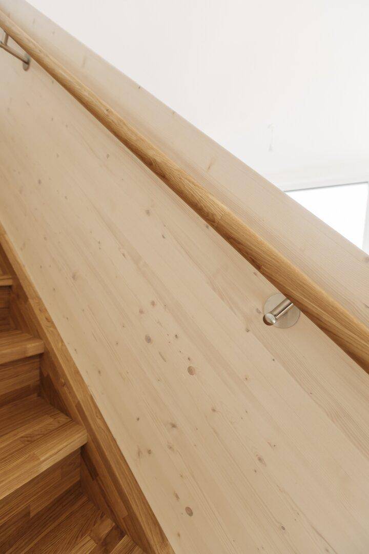 Nahaufnahme eines modernen Holzhandlaufs, der an einer hellen Wand befestigt ist.