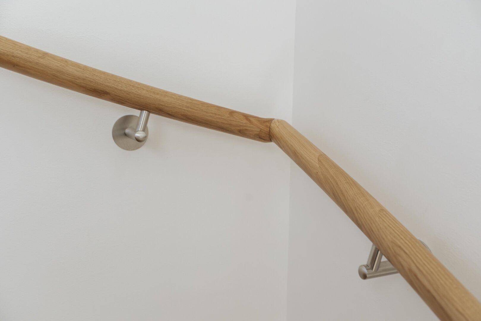 Detailansicht eines eleganten Holzhandlaufs mit Metallhalterungen an einer weißen Wand.