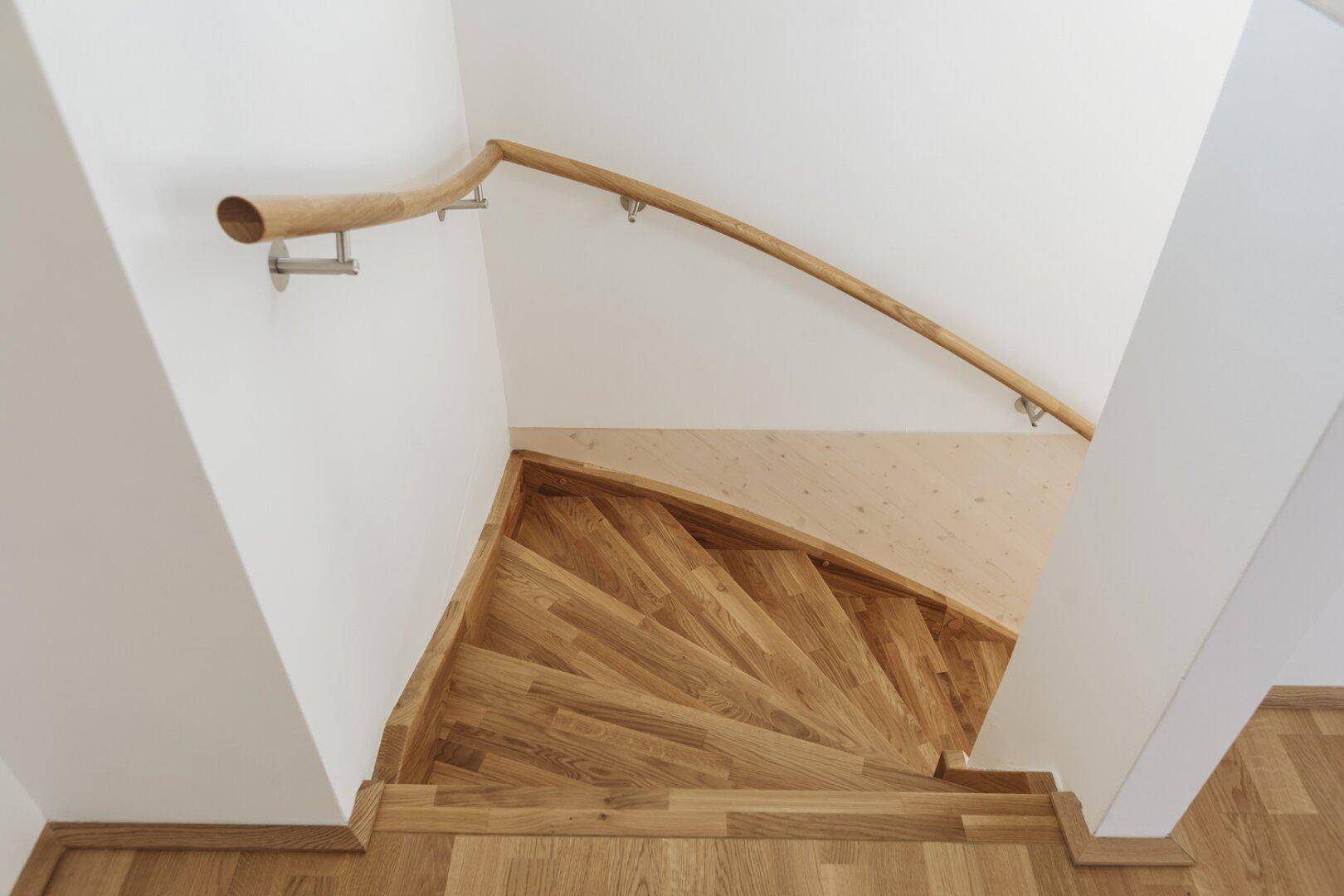 Blick von oben auf eine geschwungene Holztreppe mit Handlauf und Holzboden.