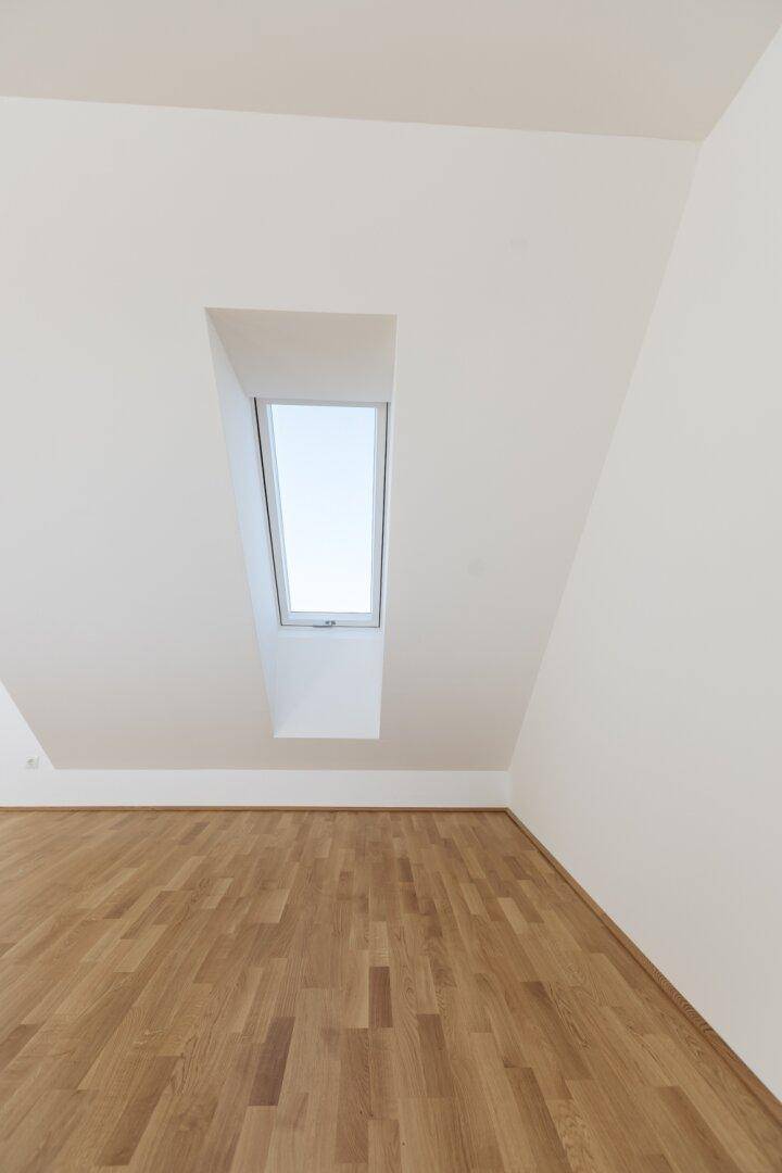Heller Raum im Dachgeschoss mit Holzboden und einem Dachfenster, das viel Licht hereinlässt.