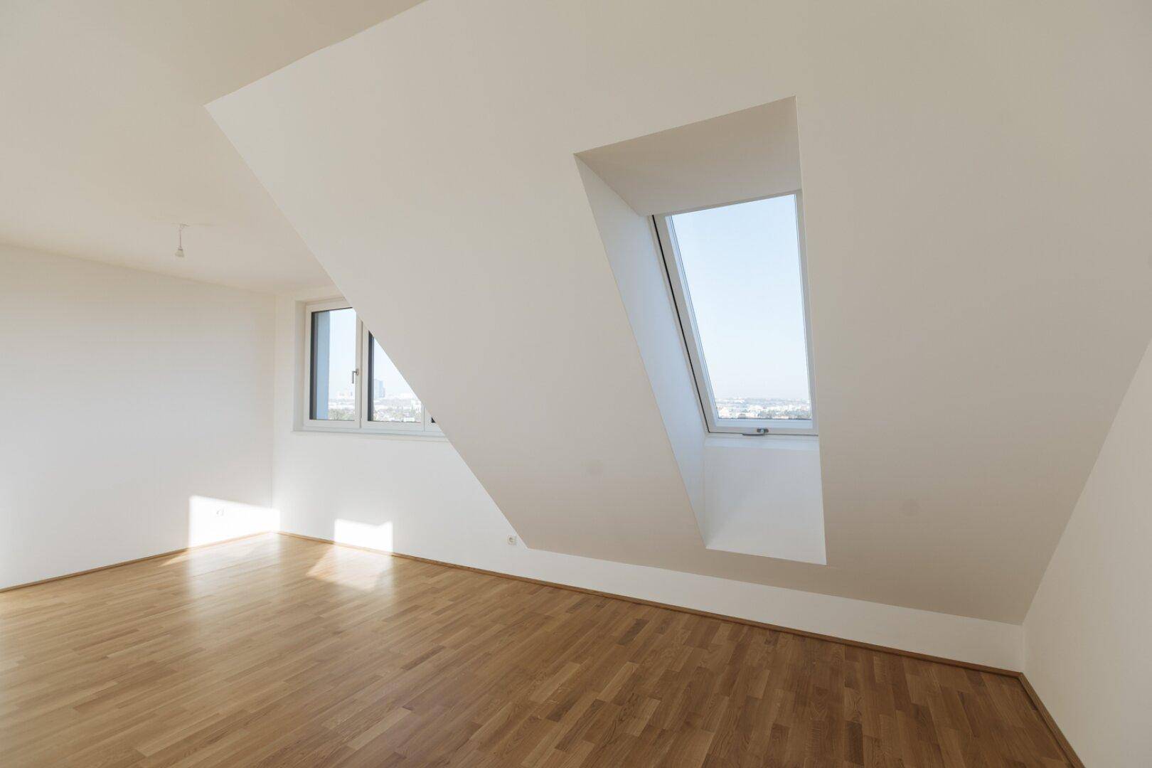 Geräumiger, heller Dachgeschossraum mit Holzboden, Dachfenster und Blick auf die Stadt.