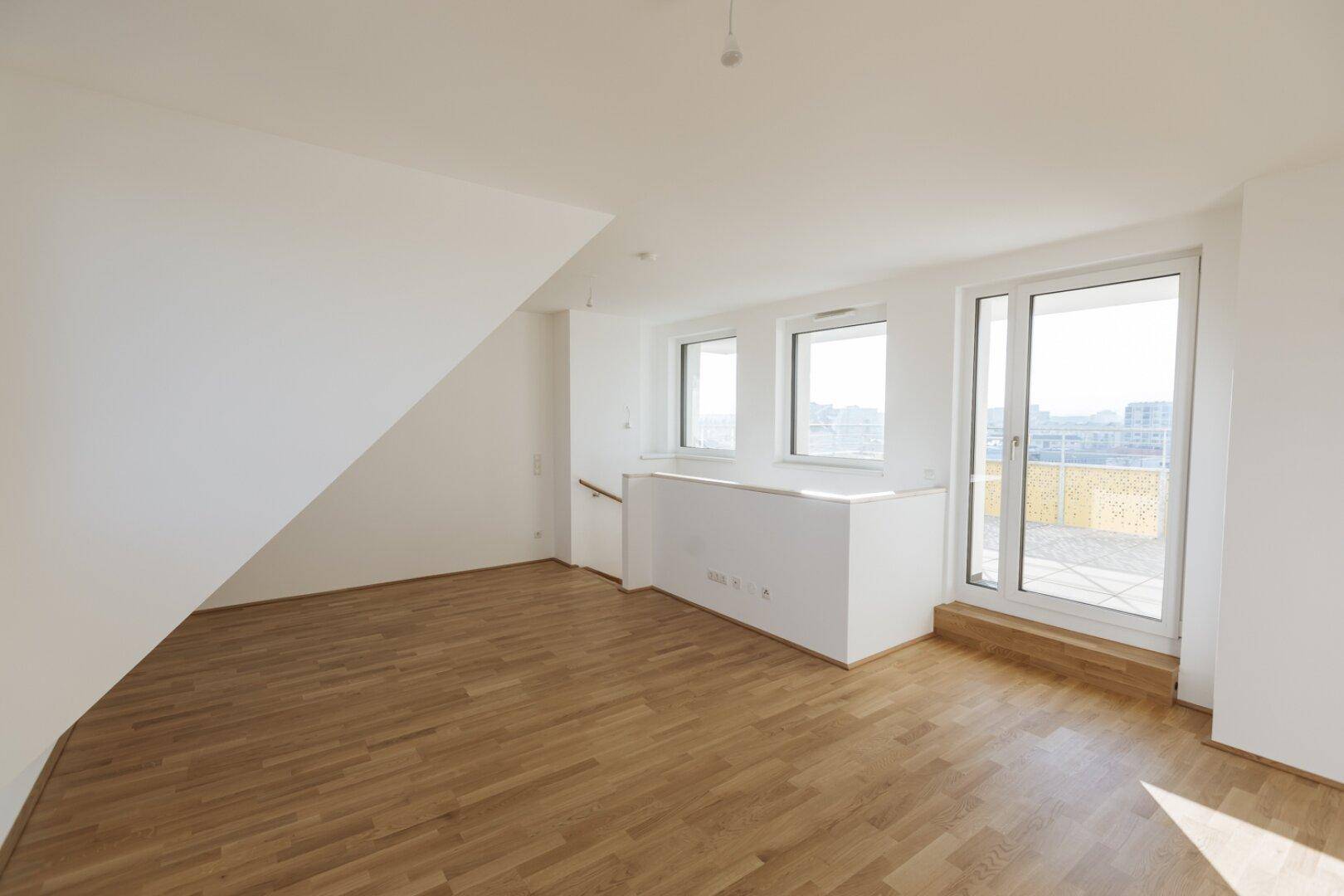 Heller Raum mit Holzboden, großen Fenstern und Zugang zu einer Terrasse, ideal für viel Tageslicht.