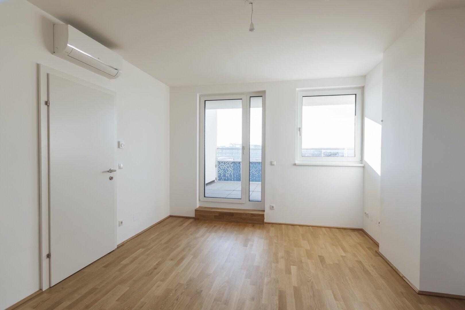Heller Raum mit Holzboden, Klimaanlage und direktem Zugang zu einem Balkon oder einer Terrasse.