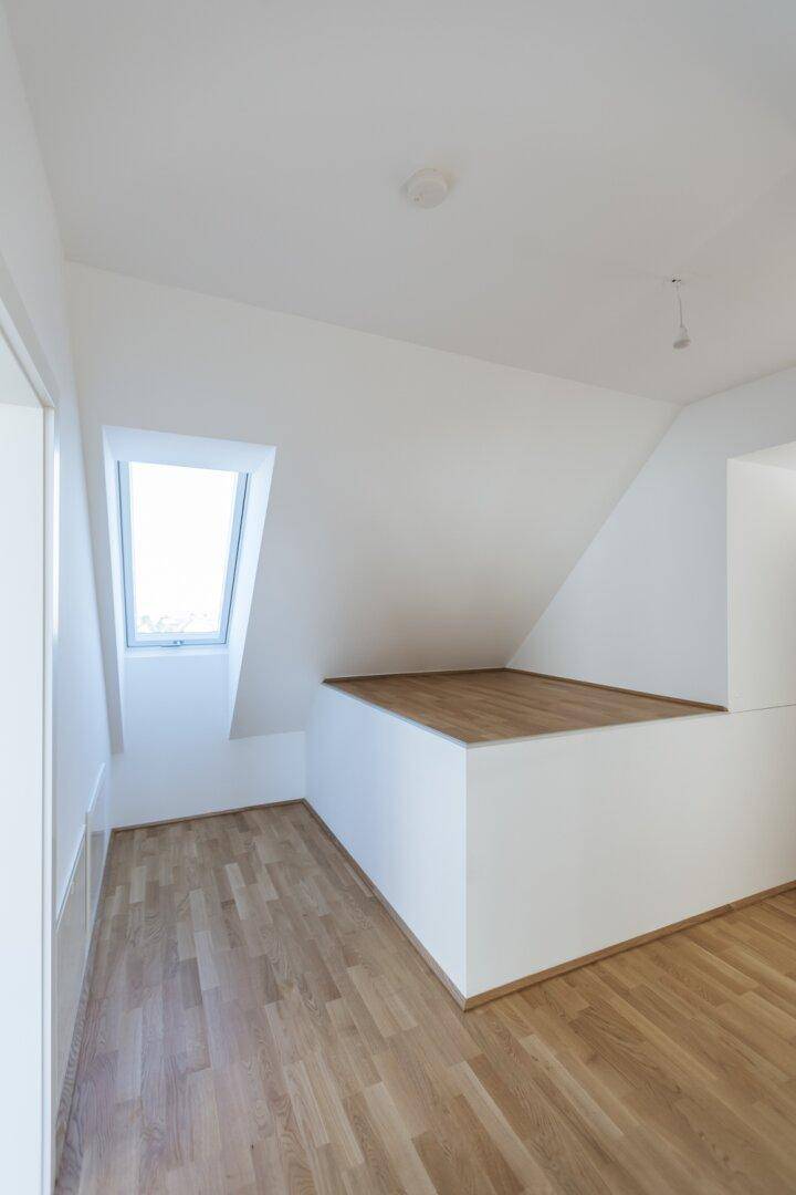 Heller Dachgeschossraum mit Holzboden, Dachfenster und einer erhöhten Plattform, die zusätzlichen Raum schafft.