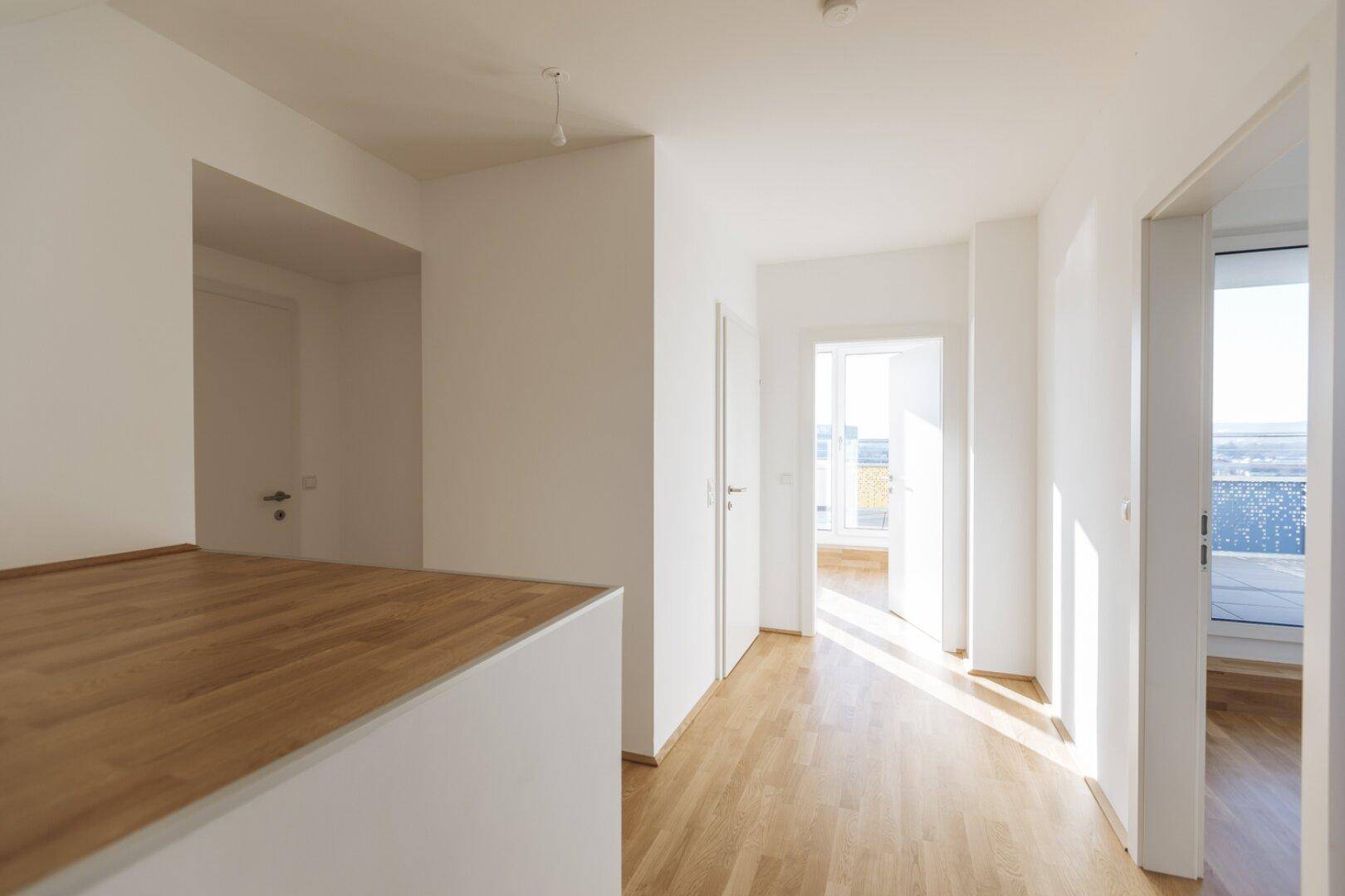 Heller Flur mit Holzboden, weißen Wänden und Zugang zu verschiedenen Räumen und einem Balkon.