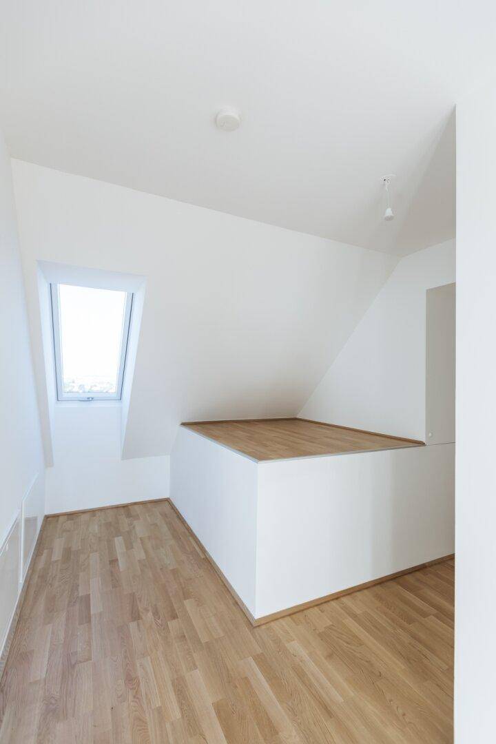 Geräumiger Dachgeschossraum mit Holzboden, Dachfenster und einer erhöhten Fläche, die vielseitig nutzbar ist.