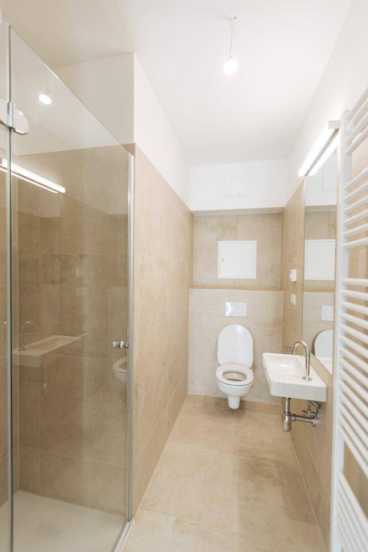 Modernes Badezimmer mit beigefarbenen Fliesen, ebenerdiger Dusche und wandhängendem WC.