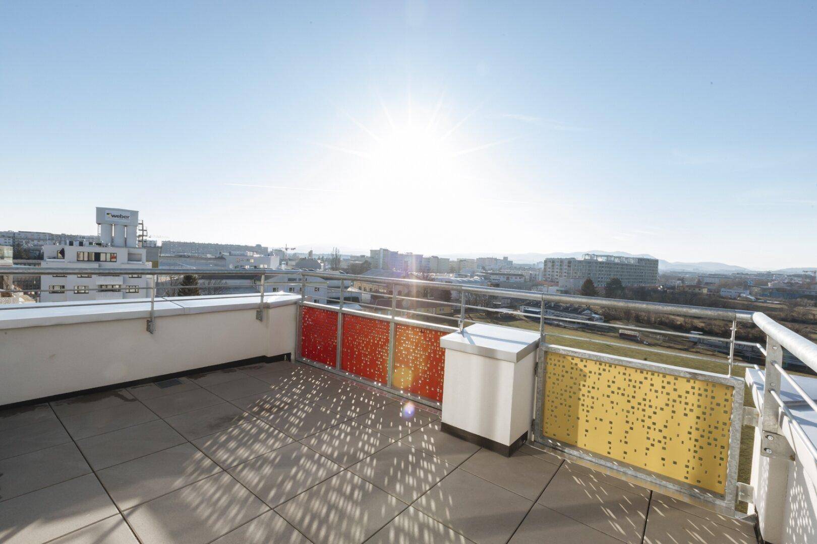 Sonnige Dachterrasse mit farbenfrohen Geländern und weitem Blick über die Stadtlandschaft.