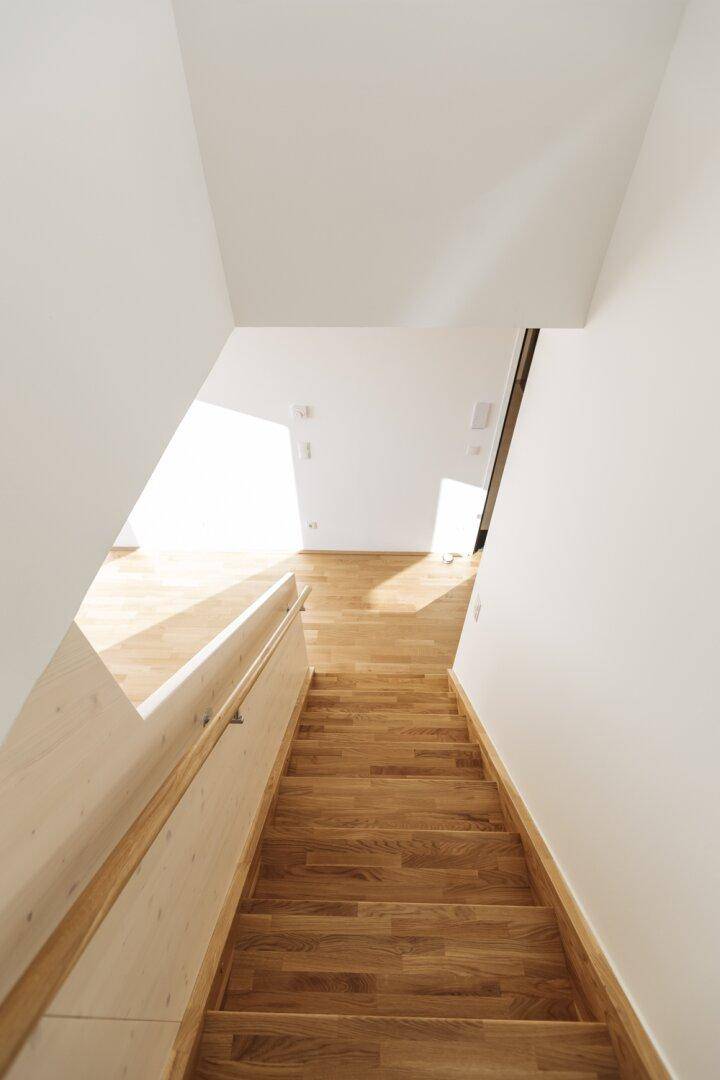 Helle Holztreppe mit Geländer, die zu einem lichtdurchfluteten Wohnbereich führt.