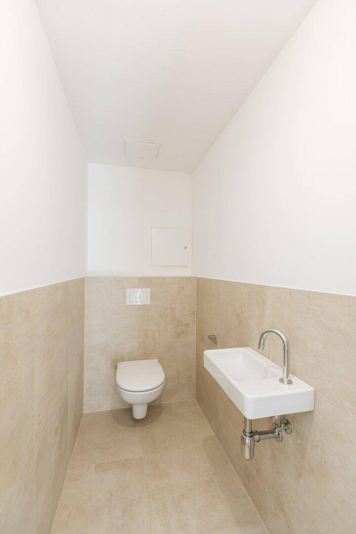 Kleines Gäste-WC mit beigefarbenen Fliesen, wandhängendem WC und modernem Handwaschbecken.