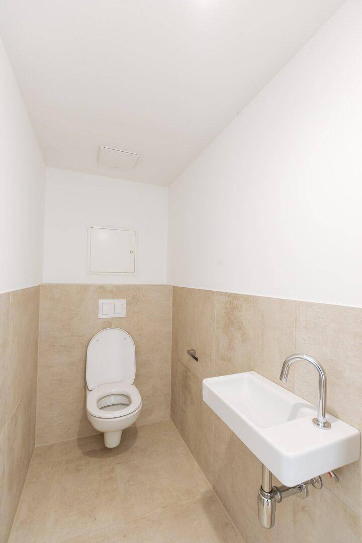Modernes Gäste-WC mit beigefarbenen Fliesen, wandhängendem WC und kleinem Waschbecken.
