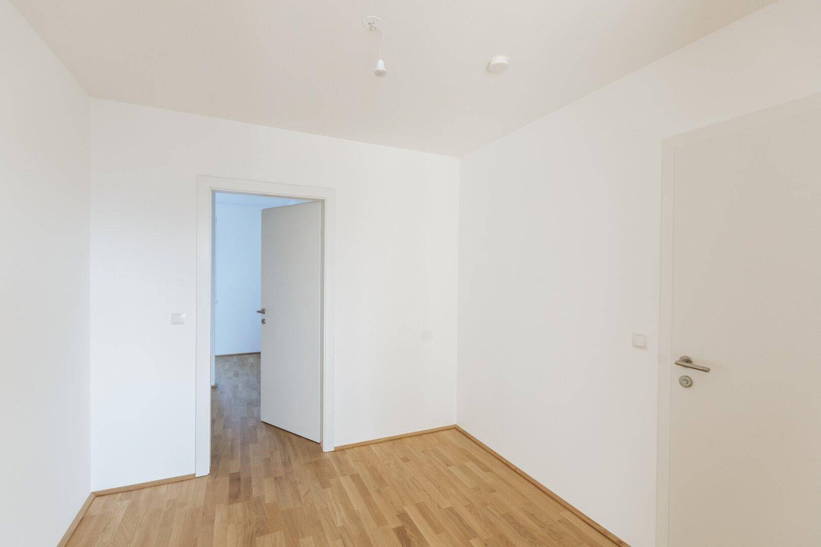 Leeres Zimmer mit Parkettboden und weiß gestrichenen Wänden, bereit zur individuellen Gestaltung.