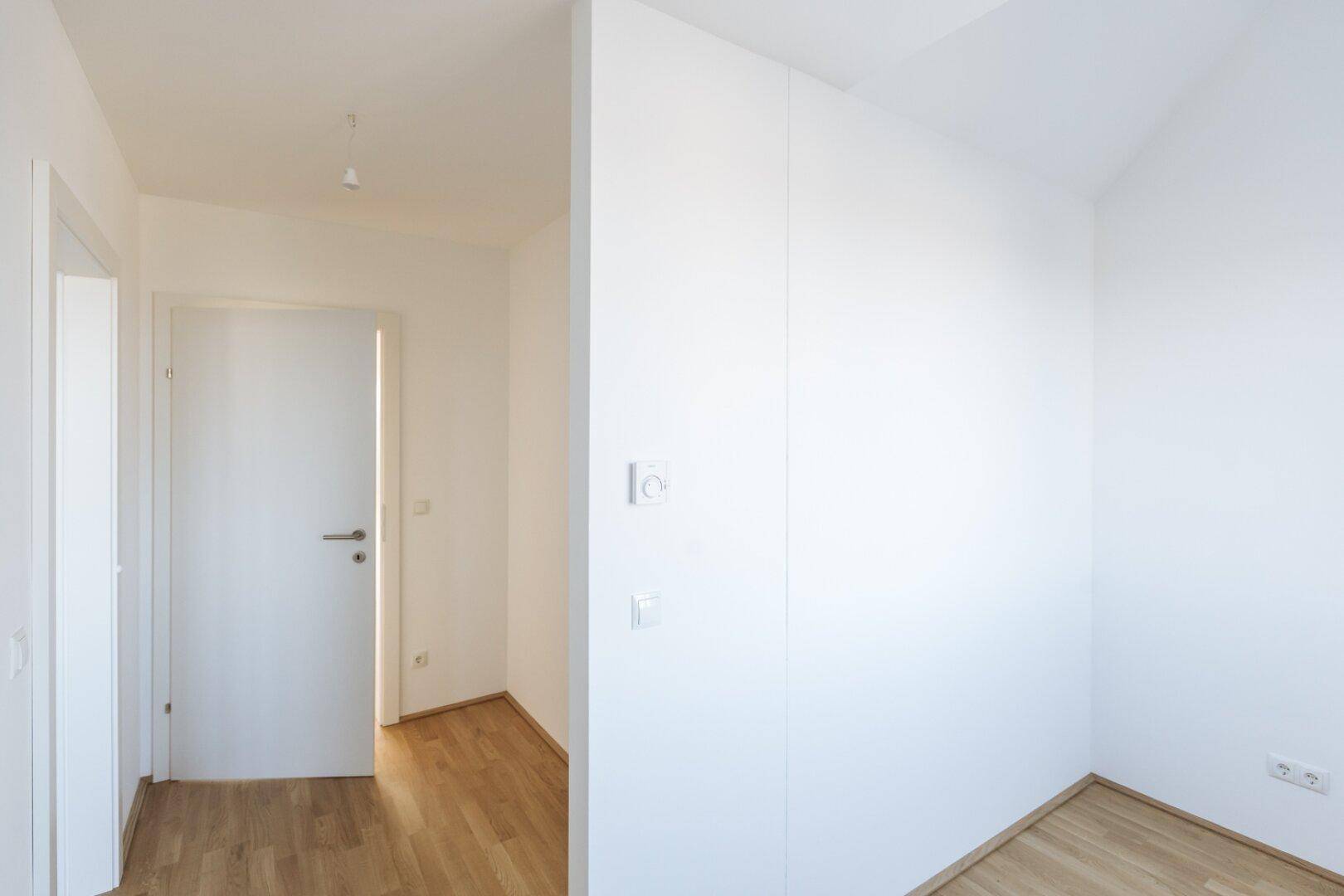 Heller Flurbereich mit Parkettboden und weißer Tür, der zu einem weiteren Zimmer führt.