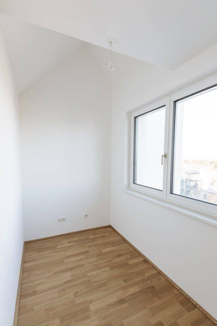 Helles Zimmer mit Dachschräge, Parkettboden und Fenster mit Weitblick.