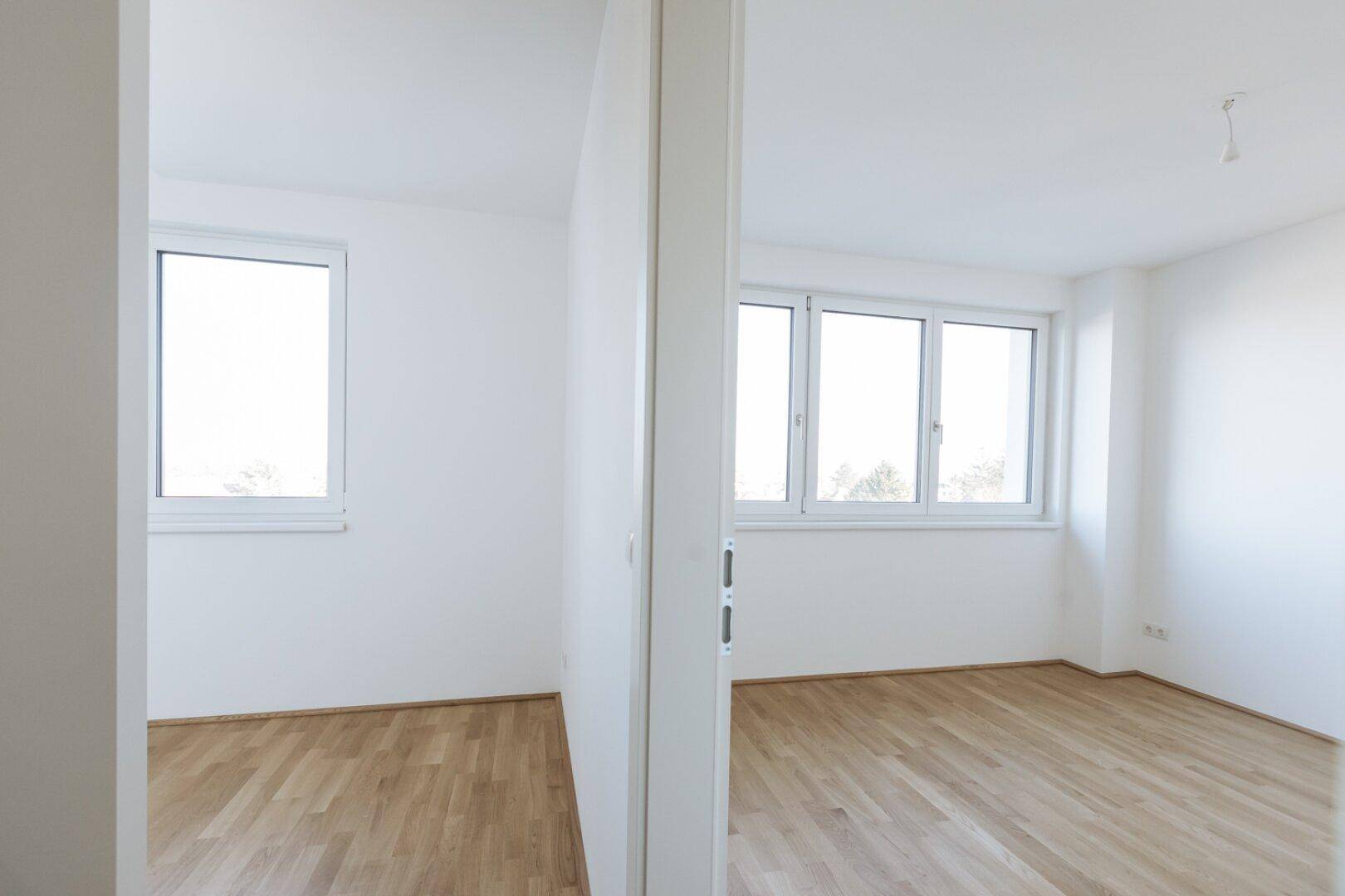 Zwei helle, leere Zimmer mit Parkettboden und großen Fenstern, ideal für Schlaf- oder Arbeitsbereiche.
