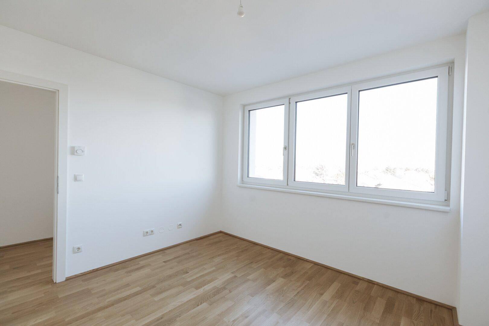 Geräumiges, helles Zimmer mit Parkettboden und drei großen Fenstern, ideal als Schlafzimmer.