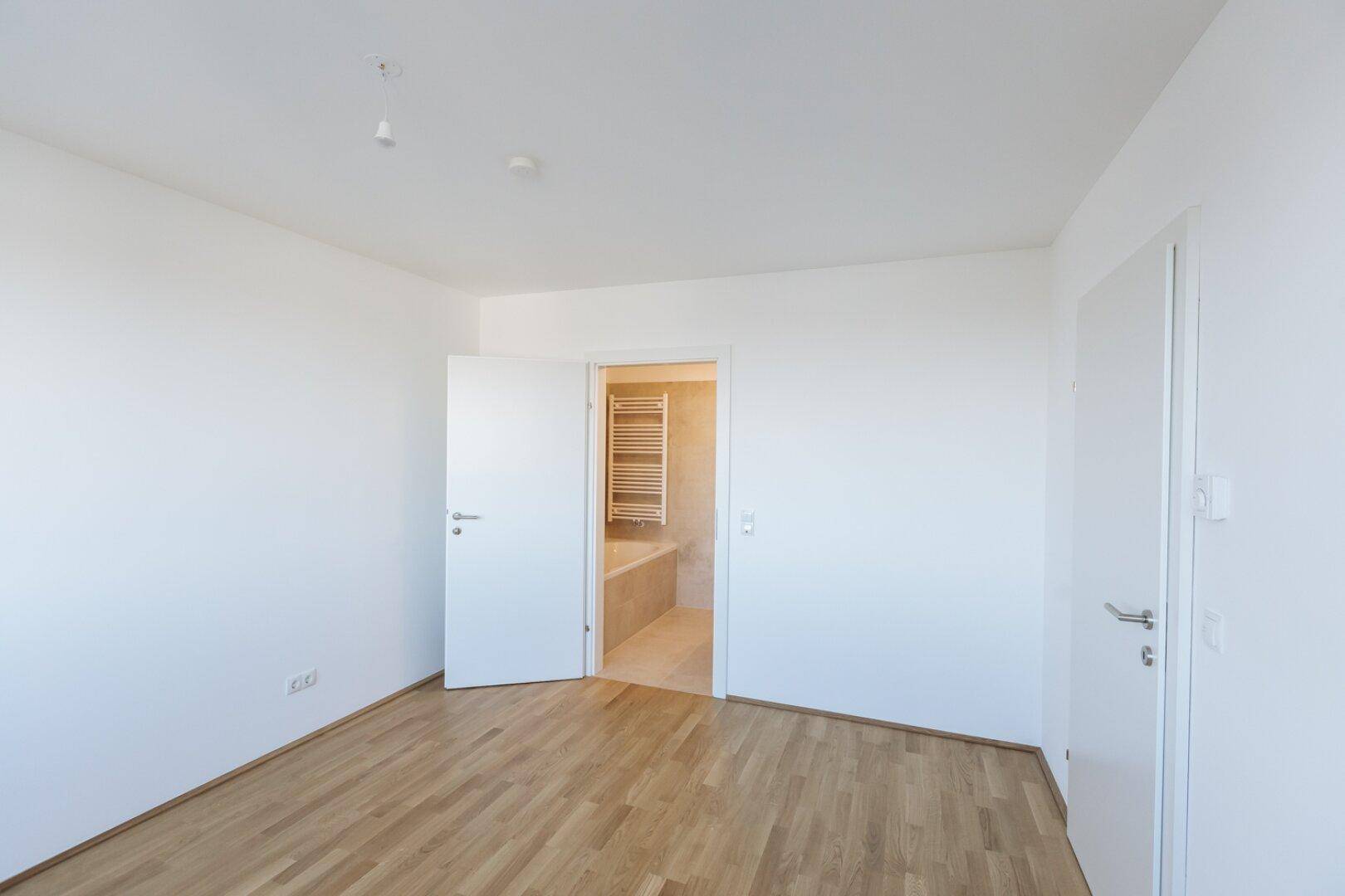 Helles Schlafzimmer mit Parkettboden und direktem Zugang zu einem Badezimmer.