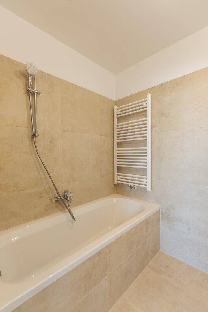 Modernes Badezimmer mit Badewanne, Duschfunktion und beheiztem Handtuchhalter.