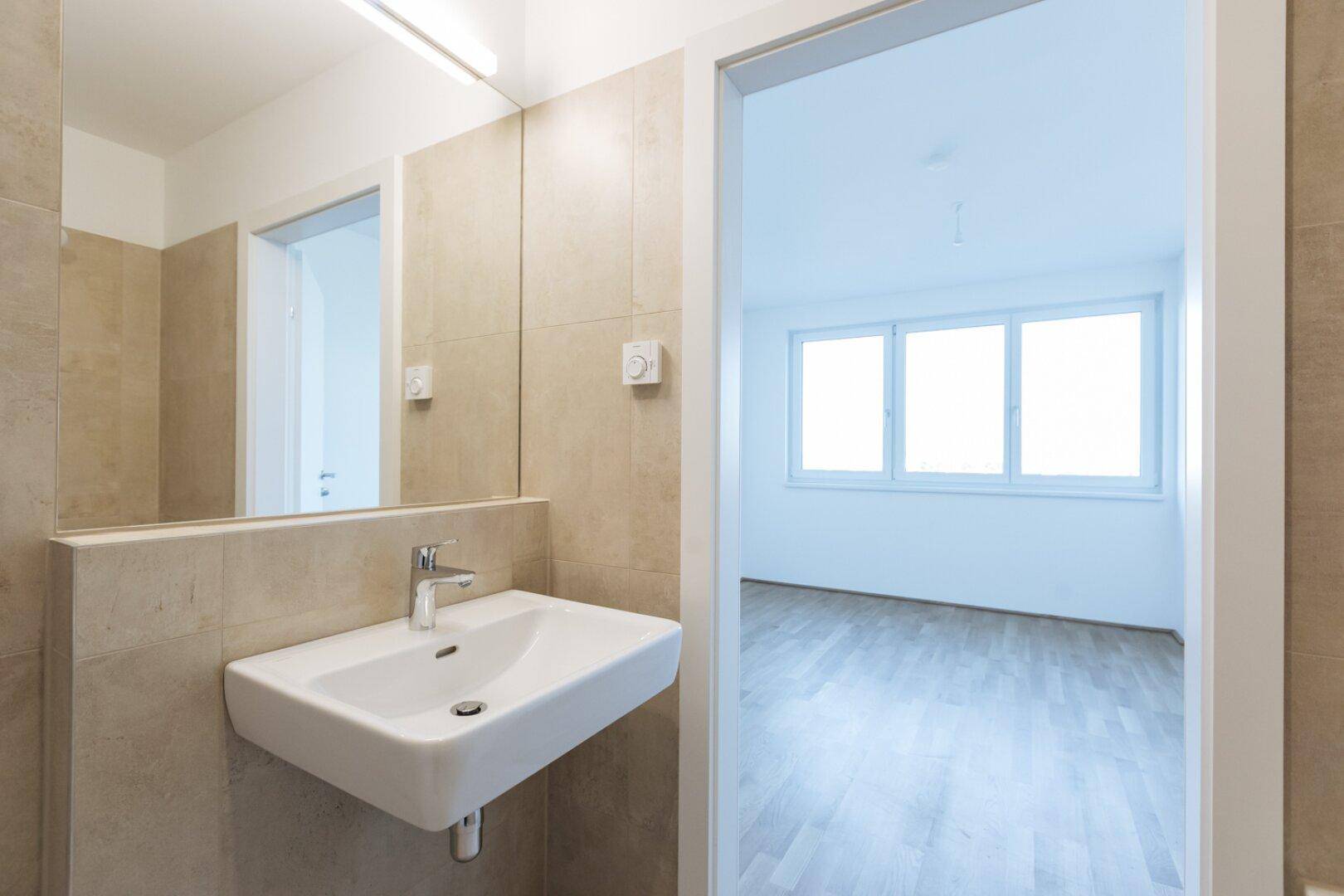 Modernes Badezimmer mit Waschbecken, Spiegel und Blick in ein angrenzendes Zimmer.