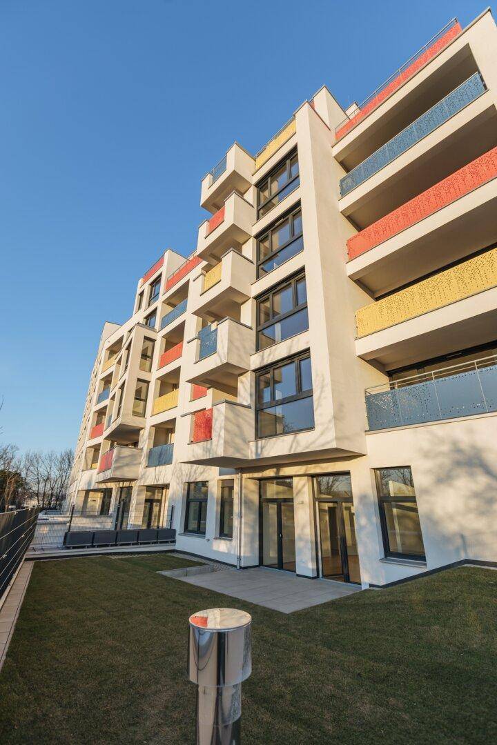 Moderne Wohnanlage mit gepflegtem Rasenbereich und farbenfrohen Balkonen.