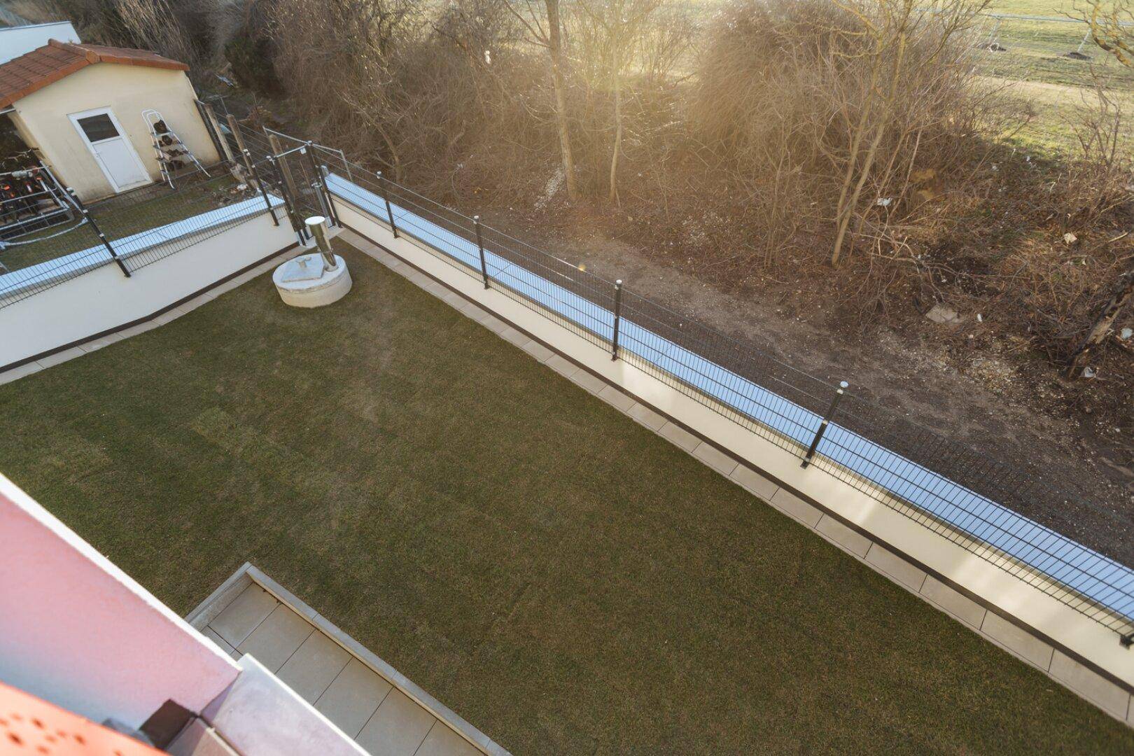 Blick von oben auf einen gepflegten Gartenbereich mit Zaun und angrenzendem Grünstreifen.