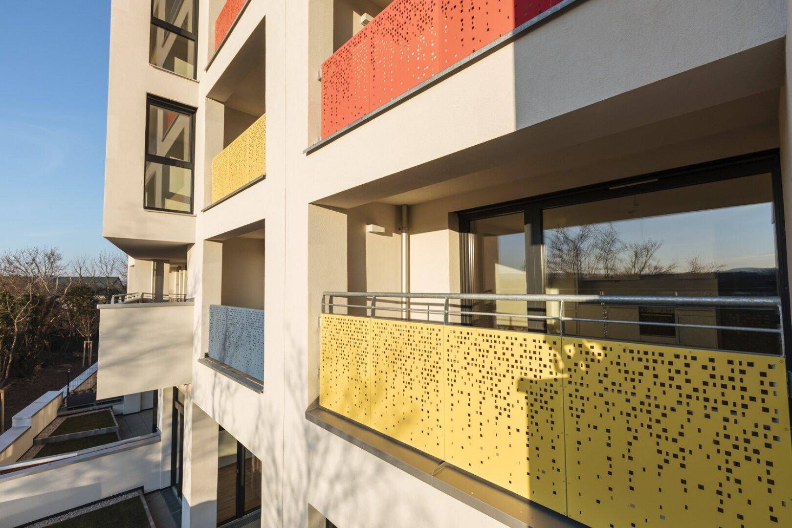 Moderner Balkon mit perforierter gelber Brüstung und Blick auf die Umgebung.