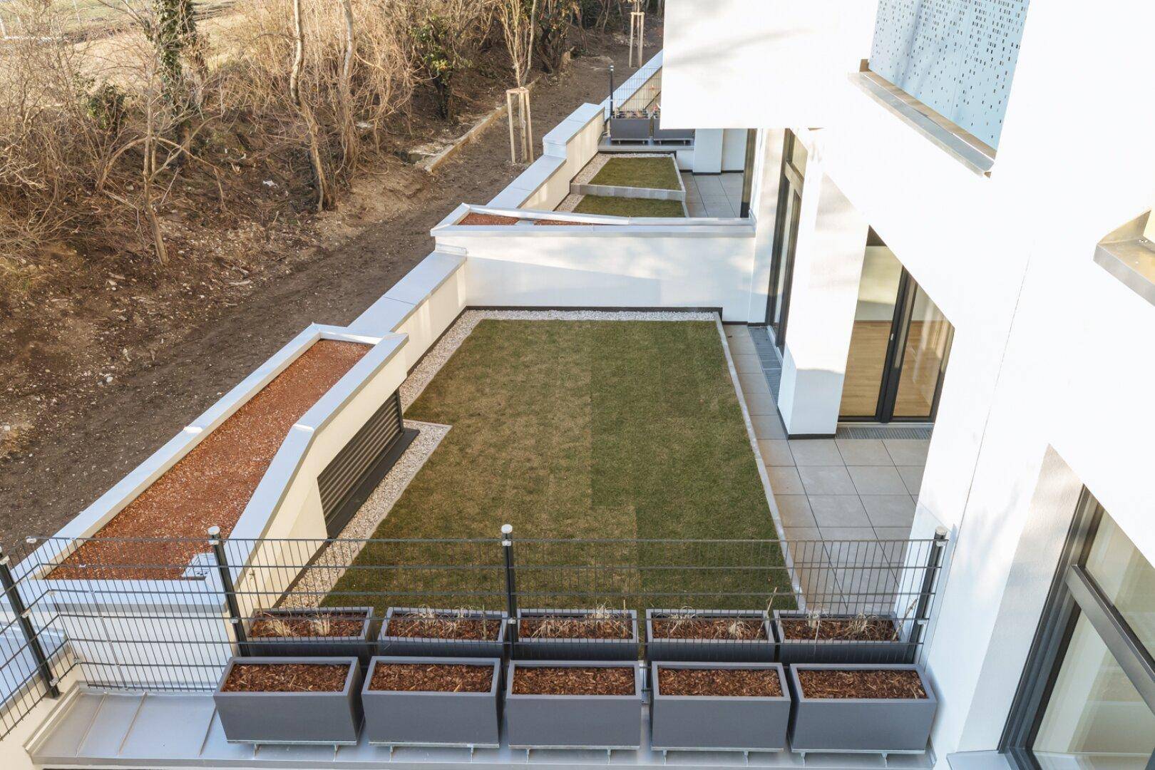 Mehrere terrassierte Gartenbereiche mit Rasen und Pflanzkübeln, von oben betrachtet.