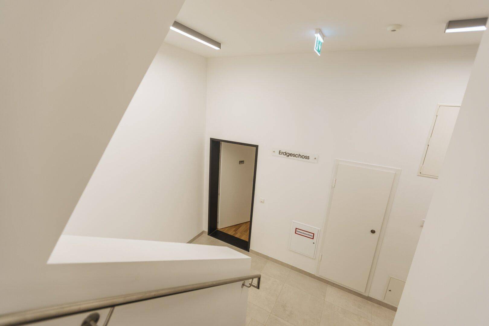 Modernes Treppenhaus mit klaren Linien und Beschilderung zum Erdgeschoss.
