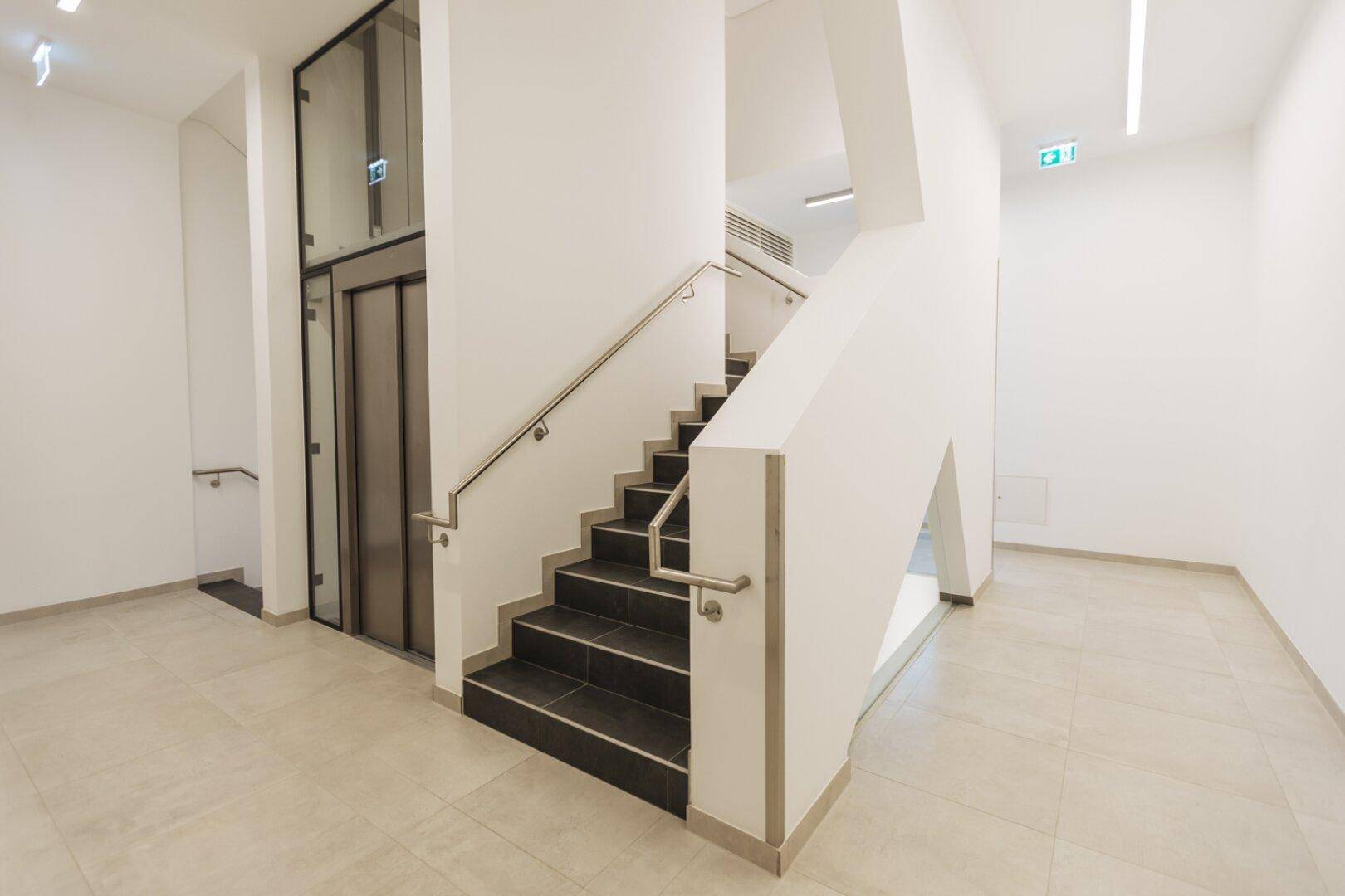 Geräumiges Treppenhaus mit Aufzug, Treppe und modernen Fliesen.
