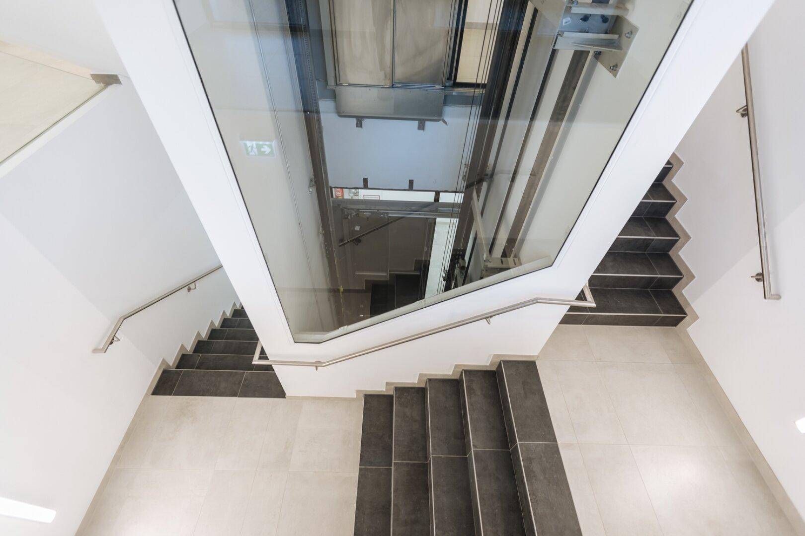 Blick von oben in ein modernes Treppenhaus mit Aufzug und Treppen.