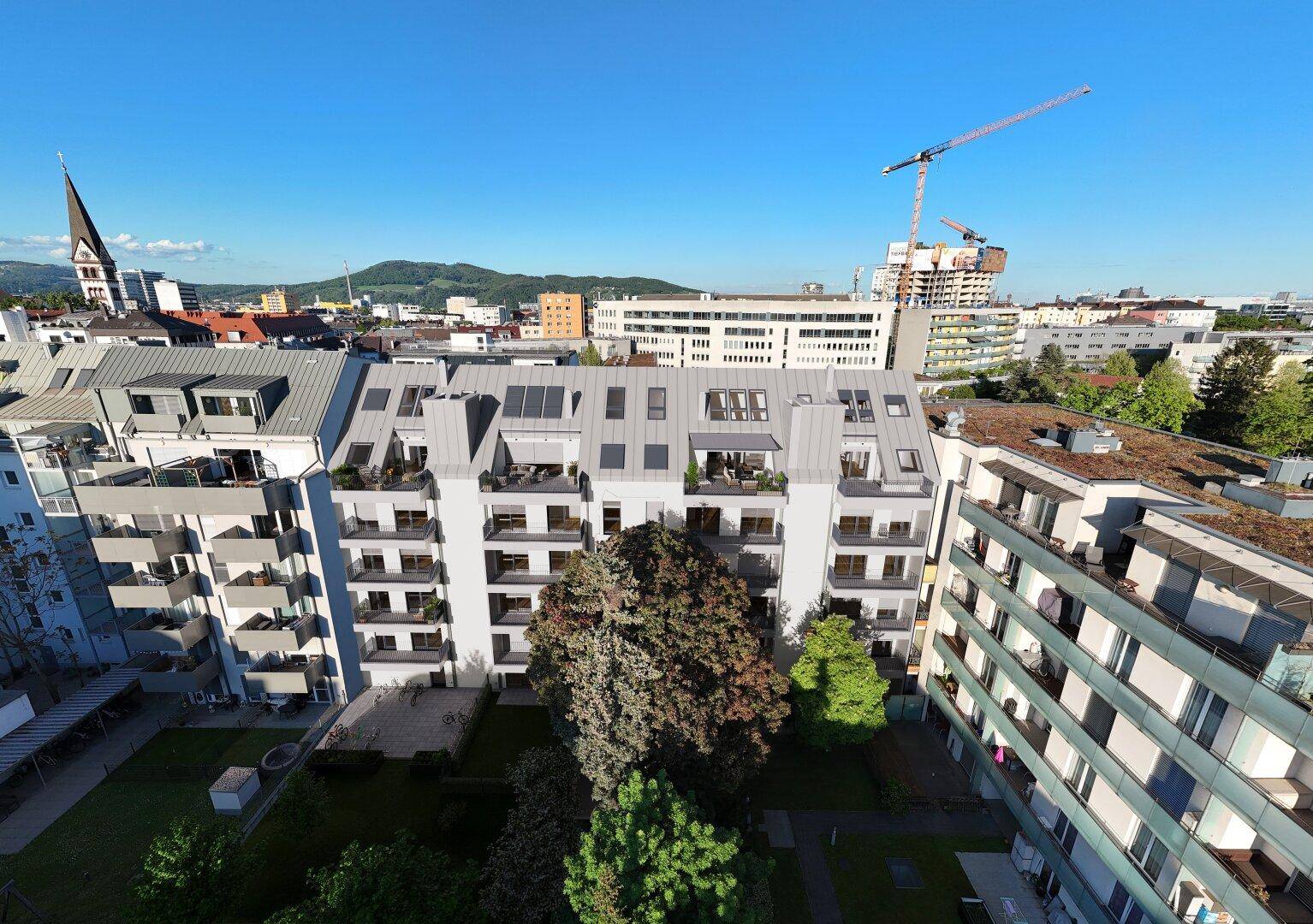 Luftaufnahme eines modernen Wohngebäudes mit Dachterrassen und umliegender Stadtlandschaft bei klarem Himmel.